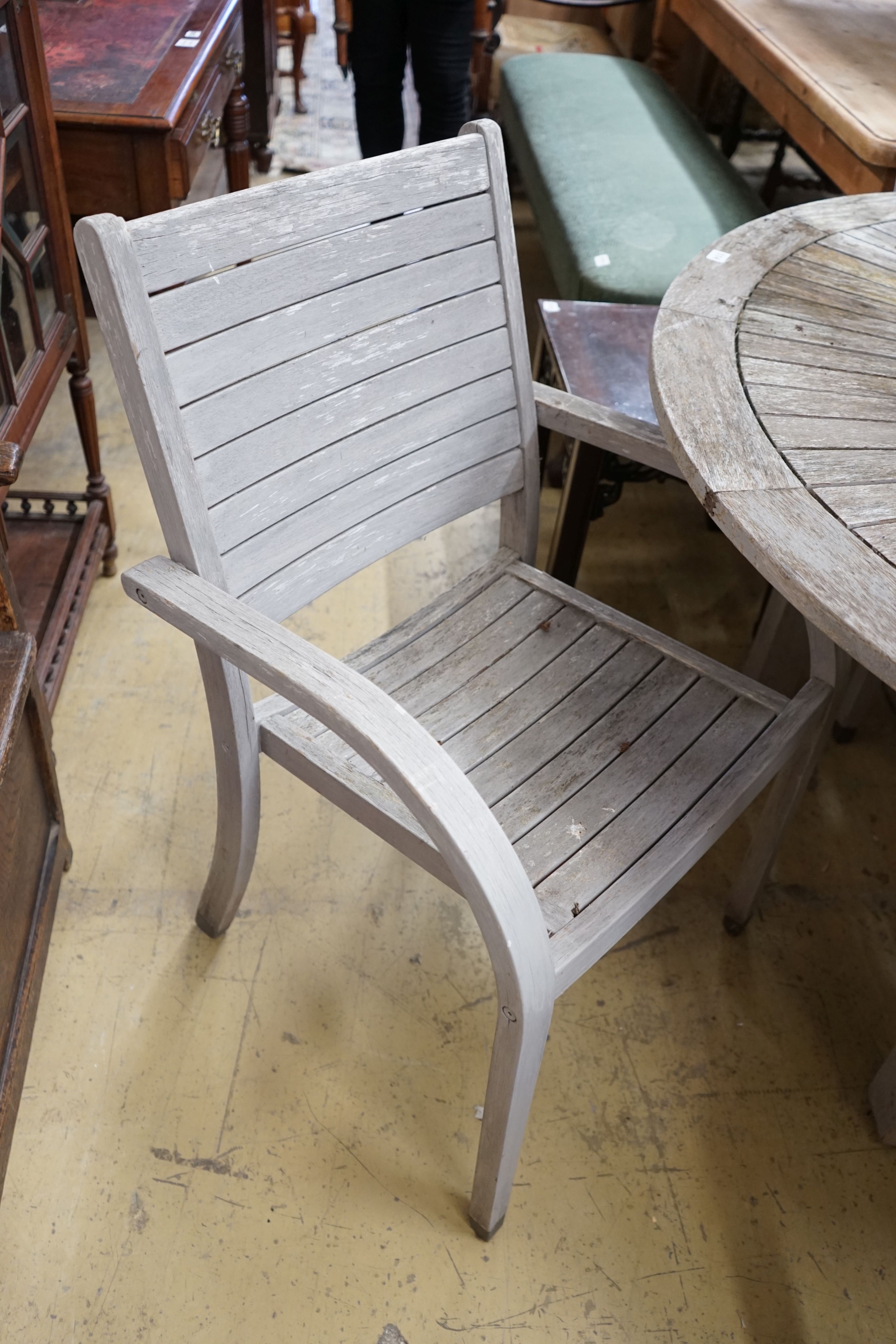 A circular weathered teak garden table, diameter 153cm, height 75cm together with six weathered teak stacking garden elbow chairs